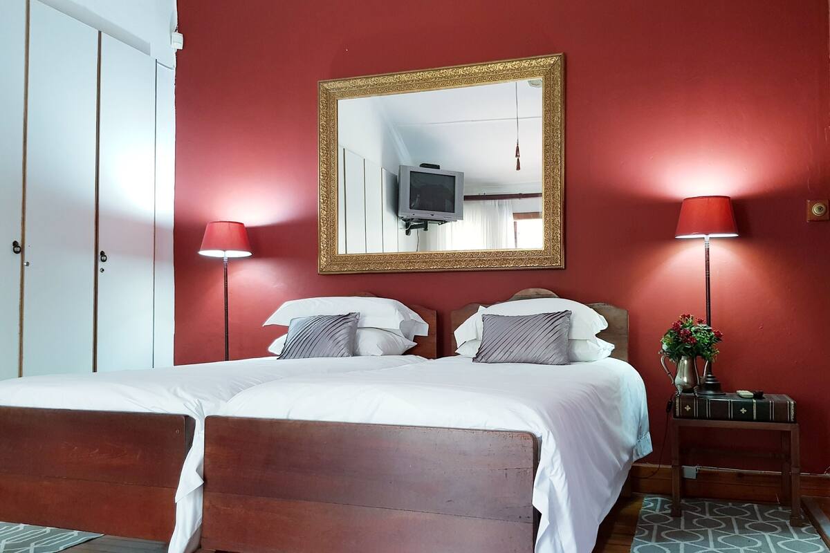 Habitación de hotel con una cama de madera, un espejo grande, un televisor y dos lámparas de noche.