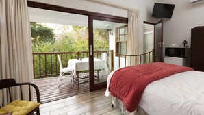 A bedroom with a bed, a TV, a desk, and a balcony with a table and chairs. - Royston Hall Guesthouse (Port Shepstone)