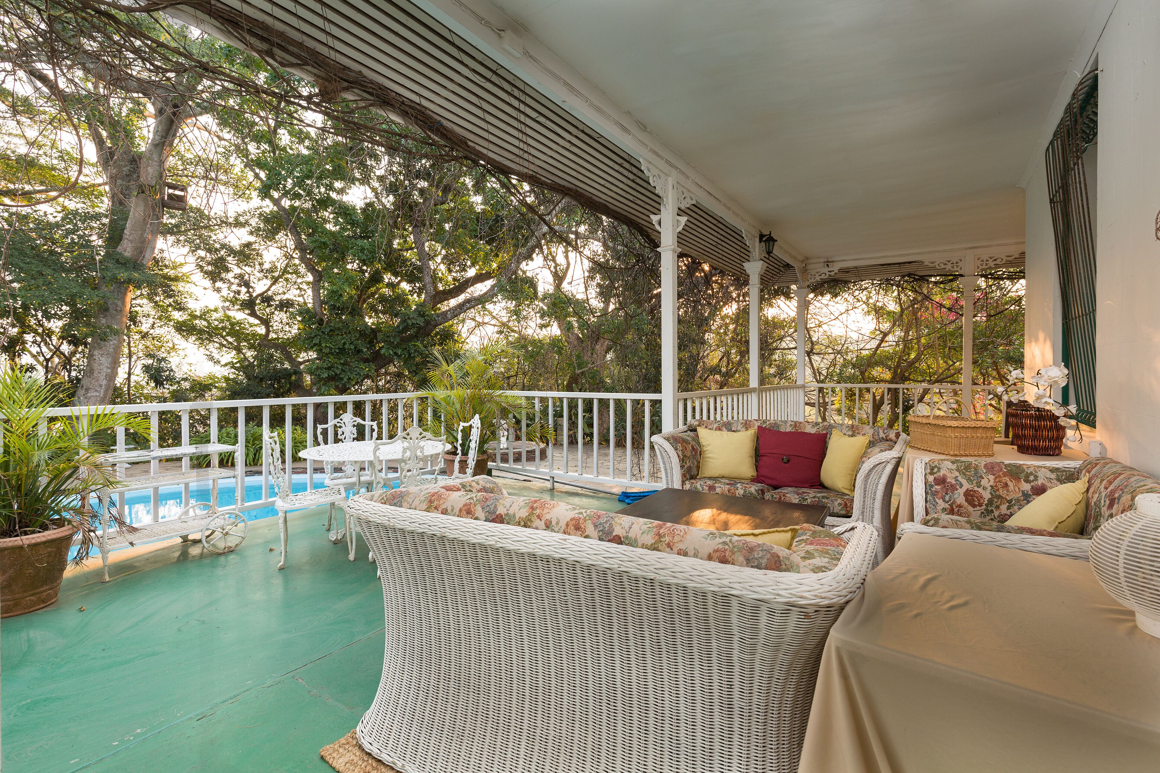 A covered outdoor seating area with wicker furniture, a pool, and potted plants.