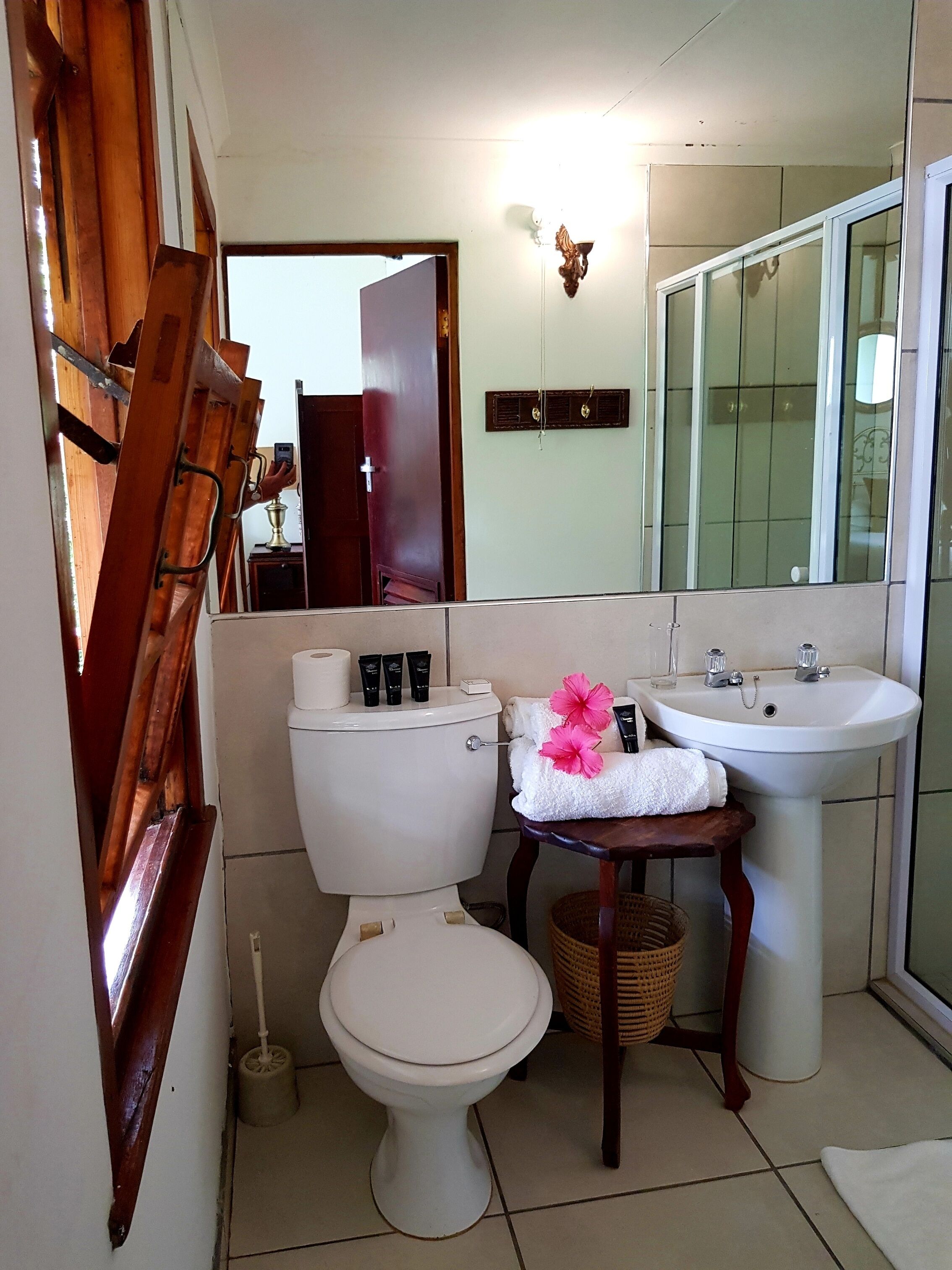 A bathroom with a toilet, sink, and mirror. There is a wooden door frame, a basket, and a towel on the sink.