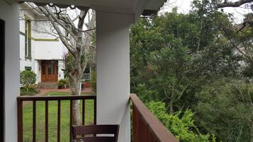 A balcony with a view of a house and dense greenery.