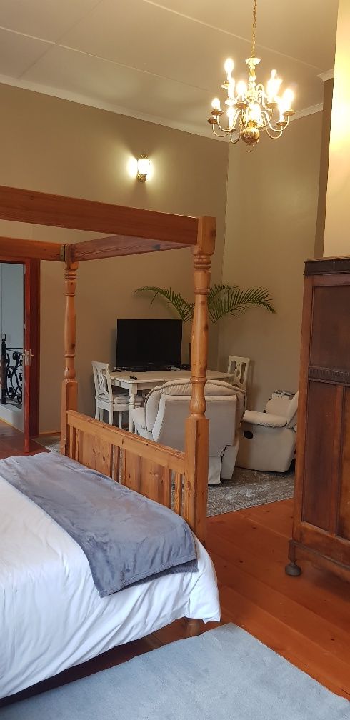 A bedroom with a four-poster bed, a chandelier, a television, and a desk with chairs.
