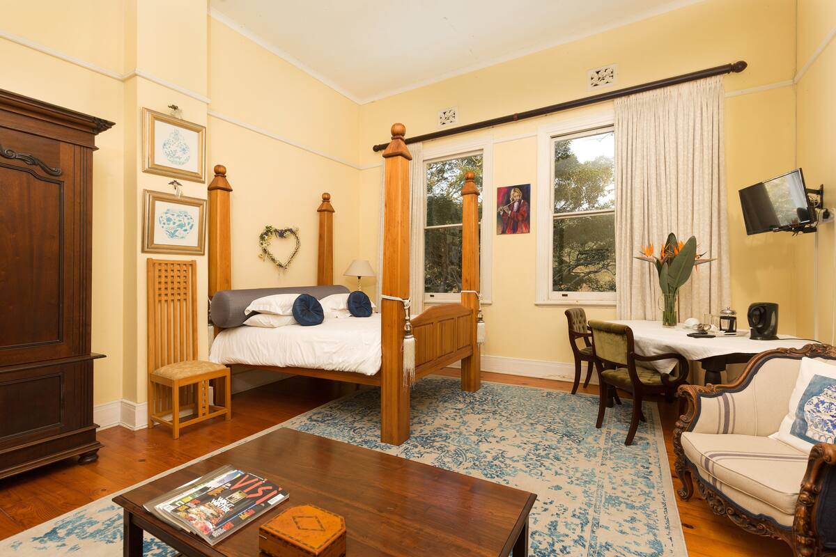 Un dormitorio con cama con dosel, un escritorio de madera, una silla y un televisor sobre un soporte.