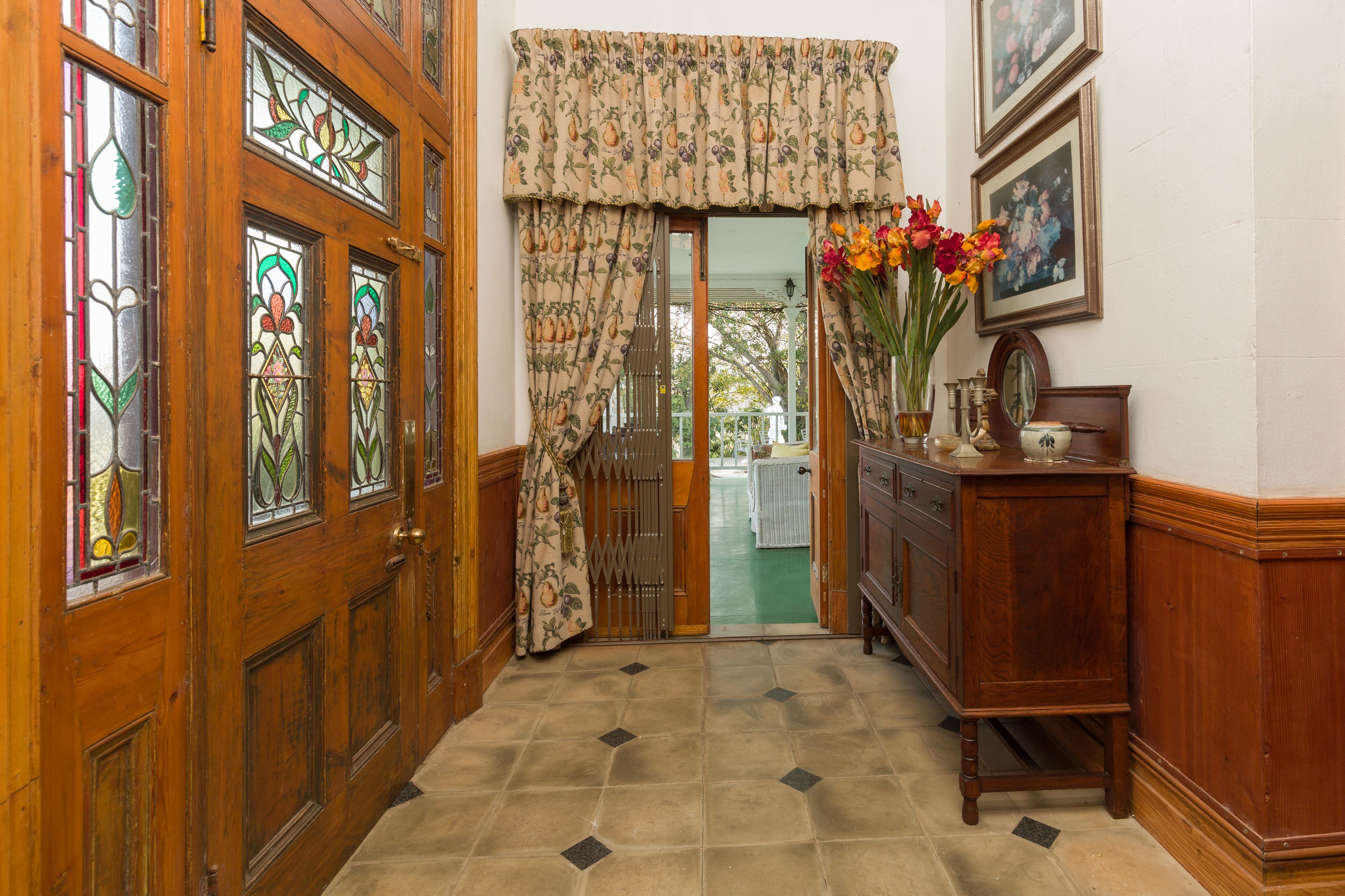 A wooden door with stained glass windows, a patterned curtain, and a vase of flowers on a wooden dresser.