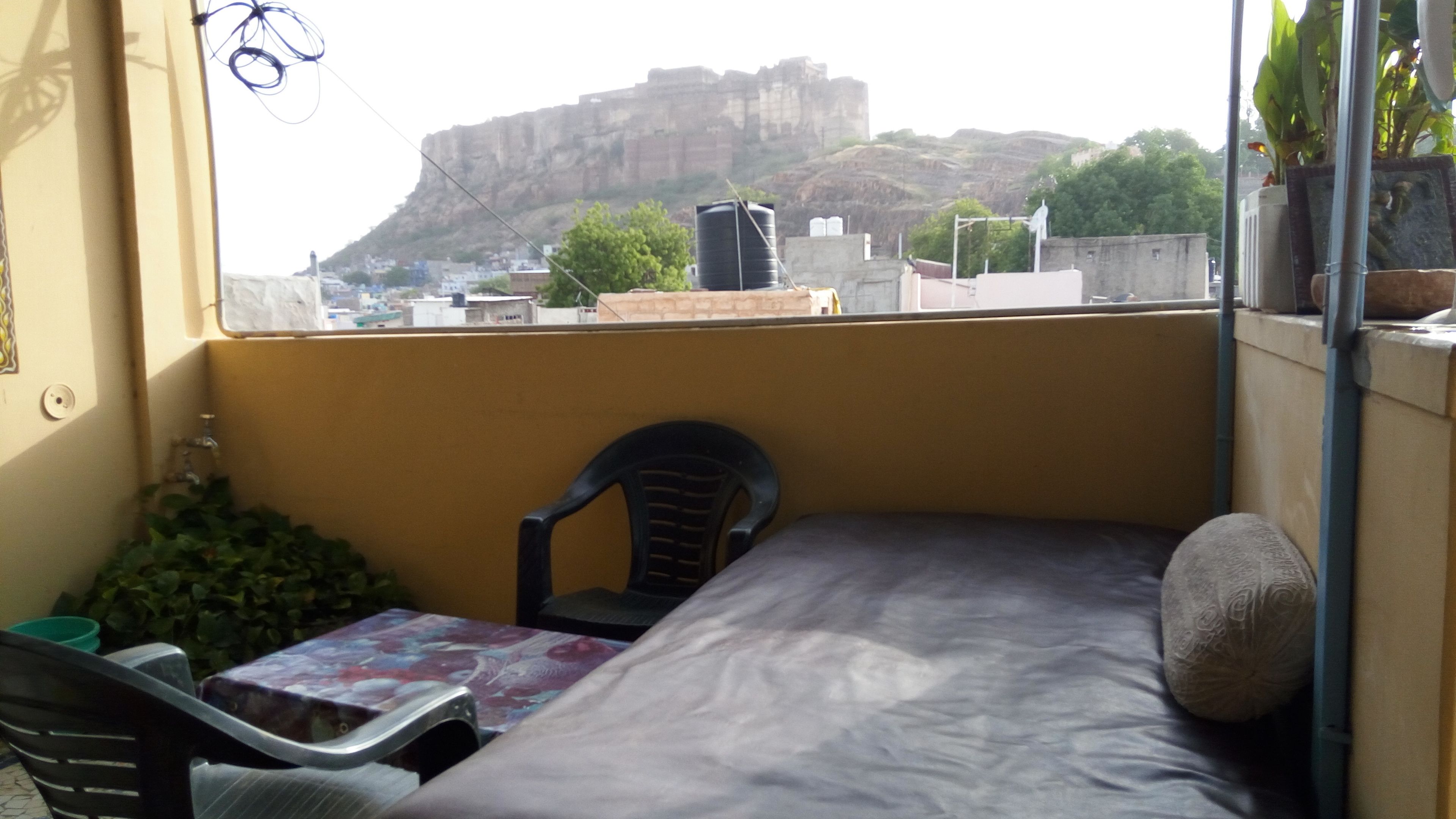 A small balcony with a bed, a chair, and a table. A large rock formation is visible in the background.