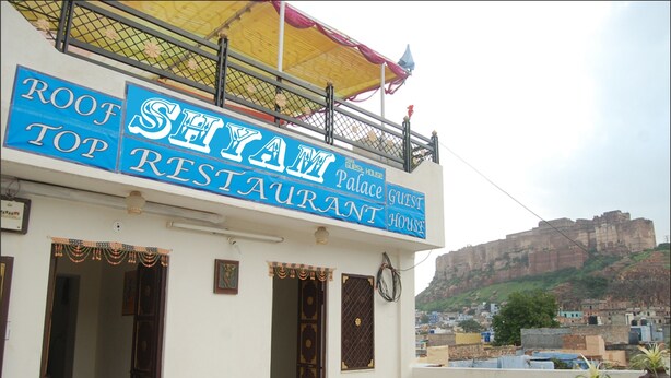 Un restaurant appelé « Root Top Restaurant », doté d’un balcon et offrant une vue sur une colline en arrière-plan.