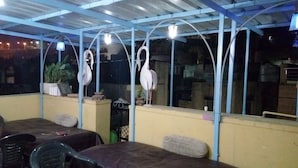 Un espace extérieur aménagé avec des tables et des chaises, protégé par une structure de toit bleue et agrémenté de luminaires suspendus.