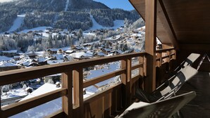 Un balcón de madera con vistas a un pueblo cubierto de nieve y montañas.