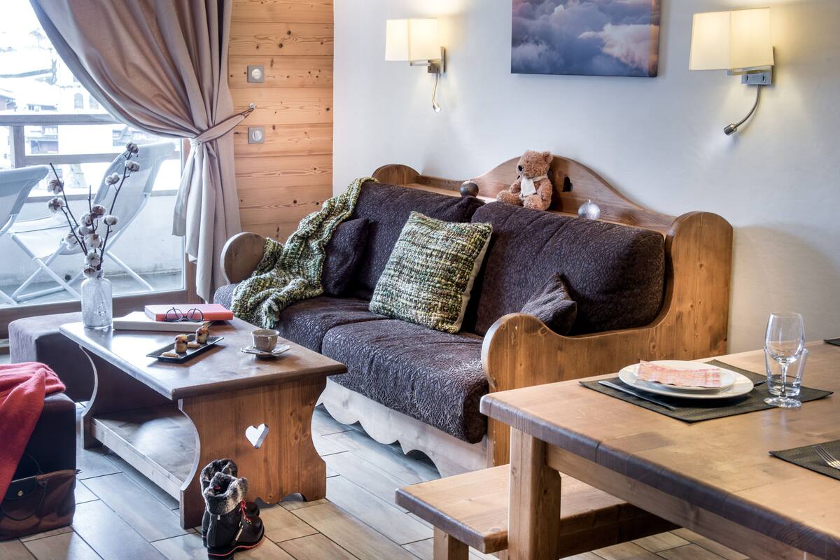 A cozy room with a wooden sofa, a small table with a cup and saucer, a bench, and a wall-mounted lamp.