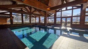 Una piscina interior con vistas claras a montañas nevadas y una estructura de techo de madera.