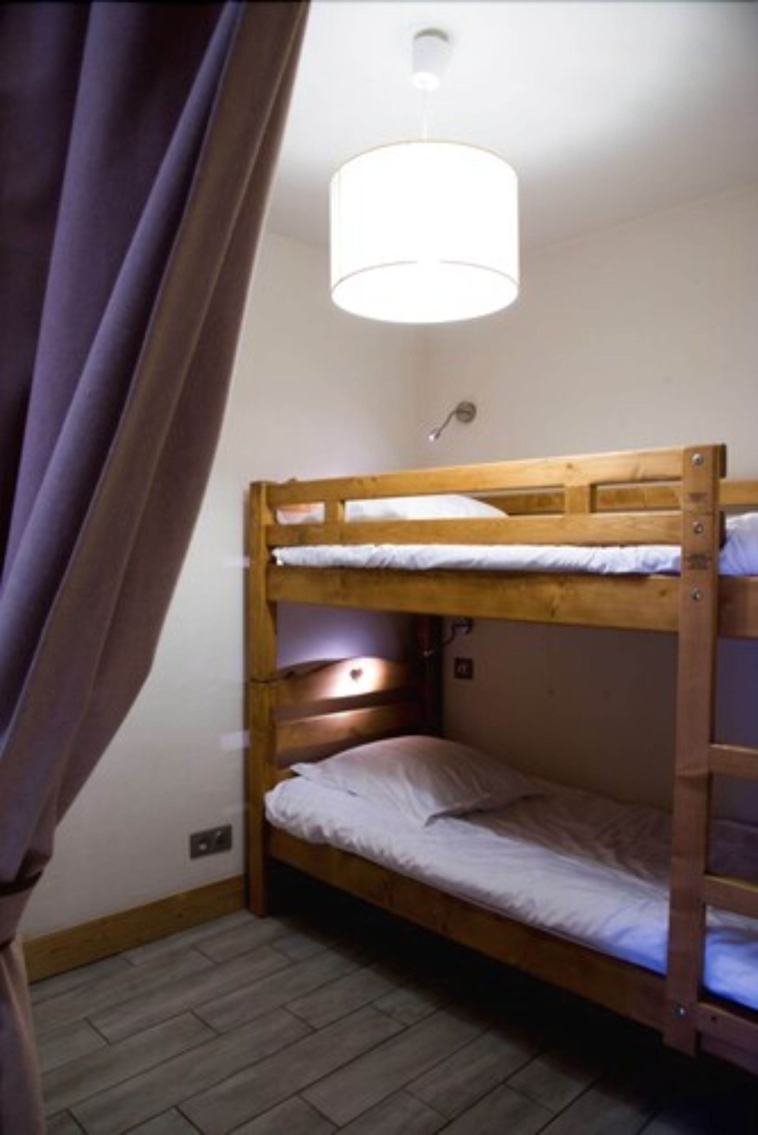 A bunk bed room with a wooden headboard, a single bed on the lower bunk, and a light fixture above.