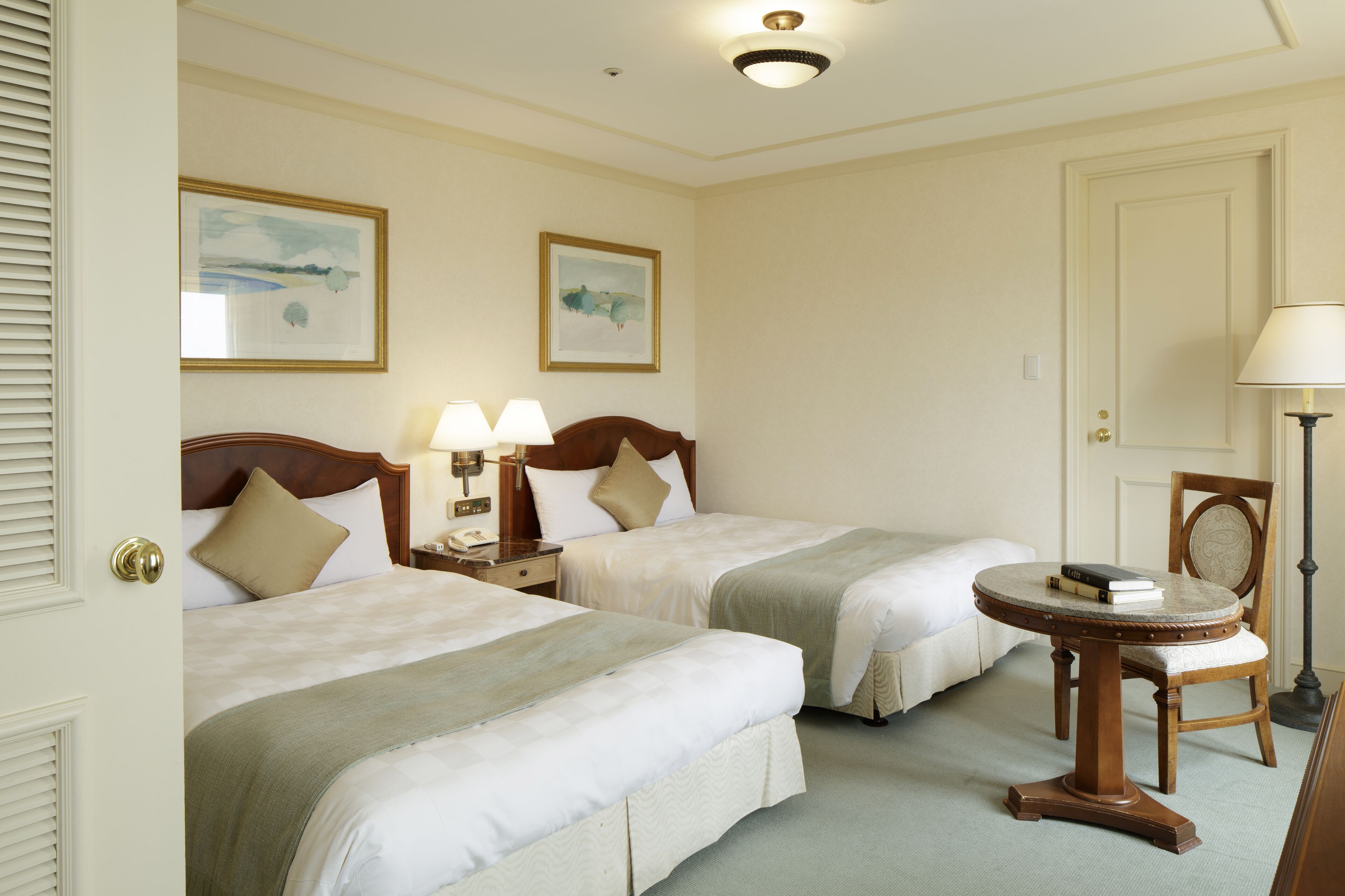 A hotel room with two beds, a round table, and two lamps.