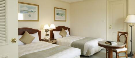 A hotel room with two beds, a round table, and two lamps.