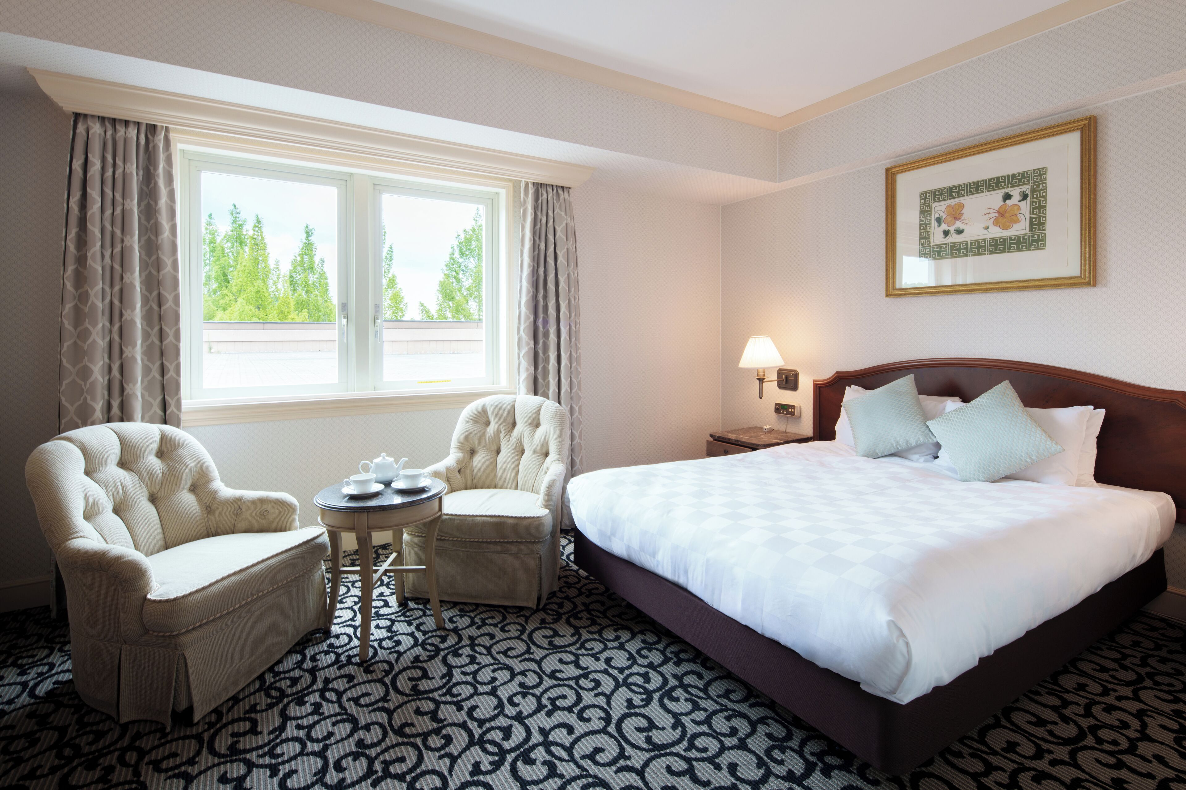 A hotel room with a large bed, two armchairs, a small table, and a window with curtains.