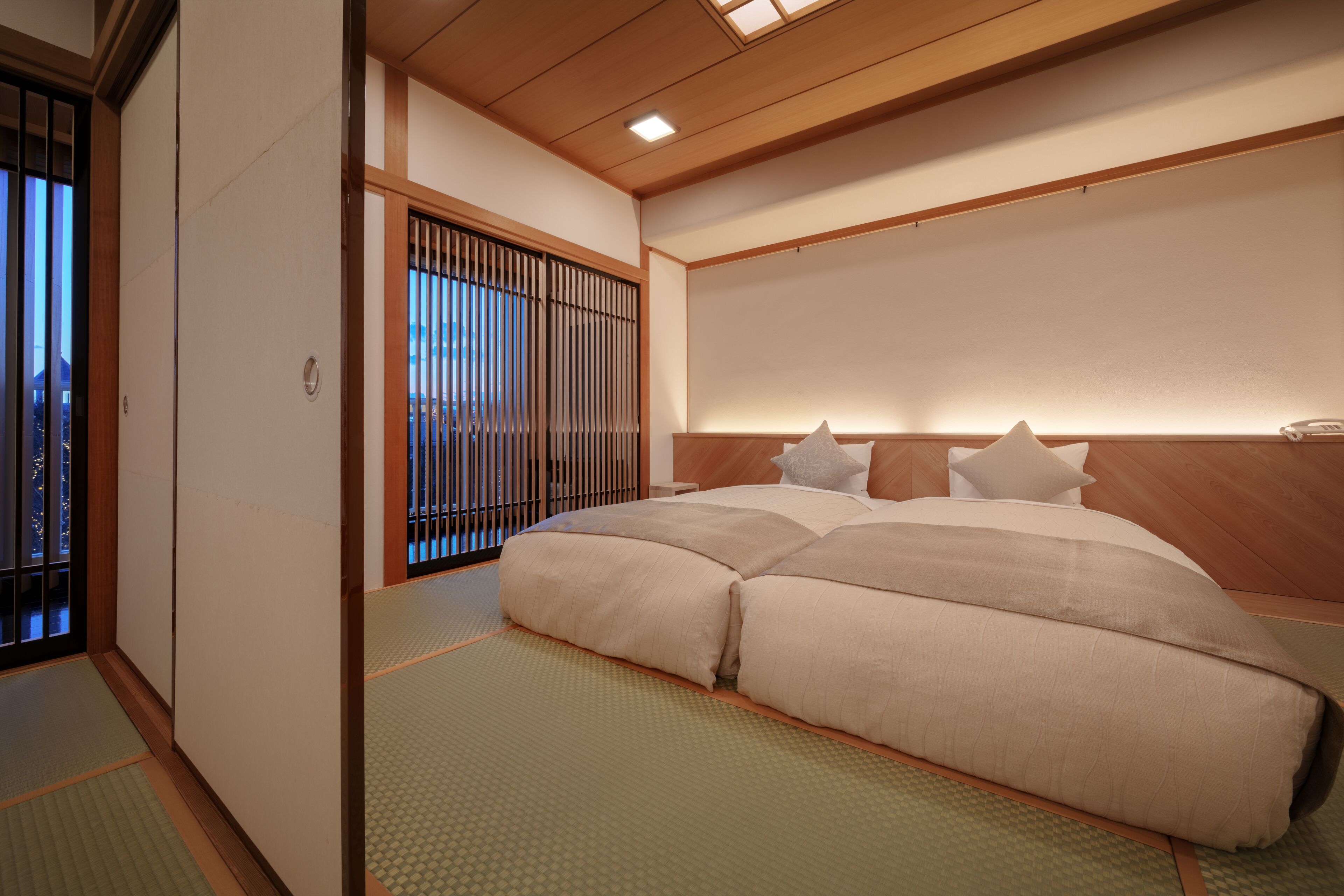 A traditional Japanese-style bedroom with tatami flooring, a low wooden bed frame, and shoji screens.