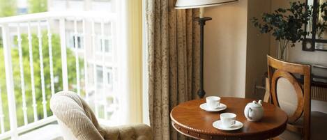 A hotel room with a balcony, a round wooden table with a teapot and cups, a chair, and a lamp.