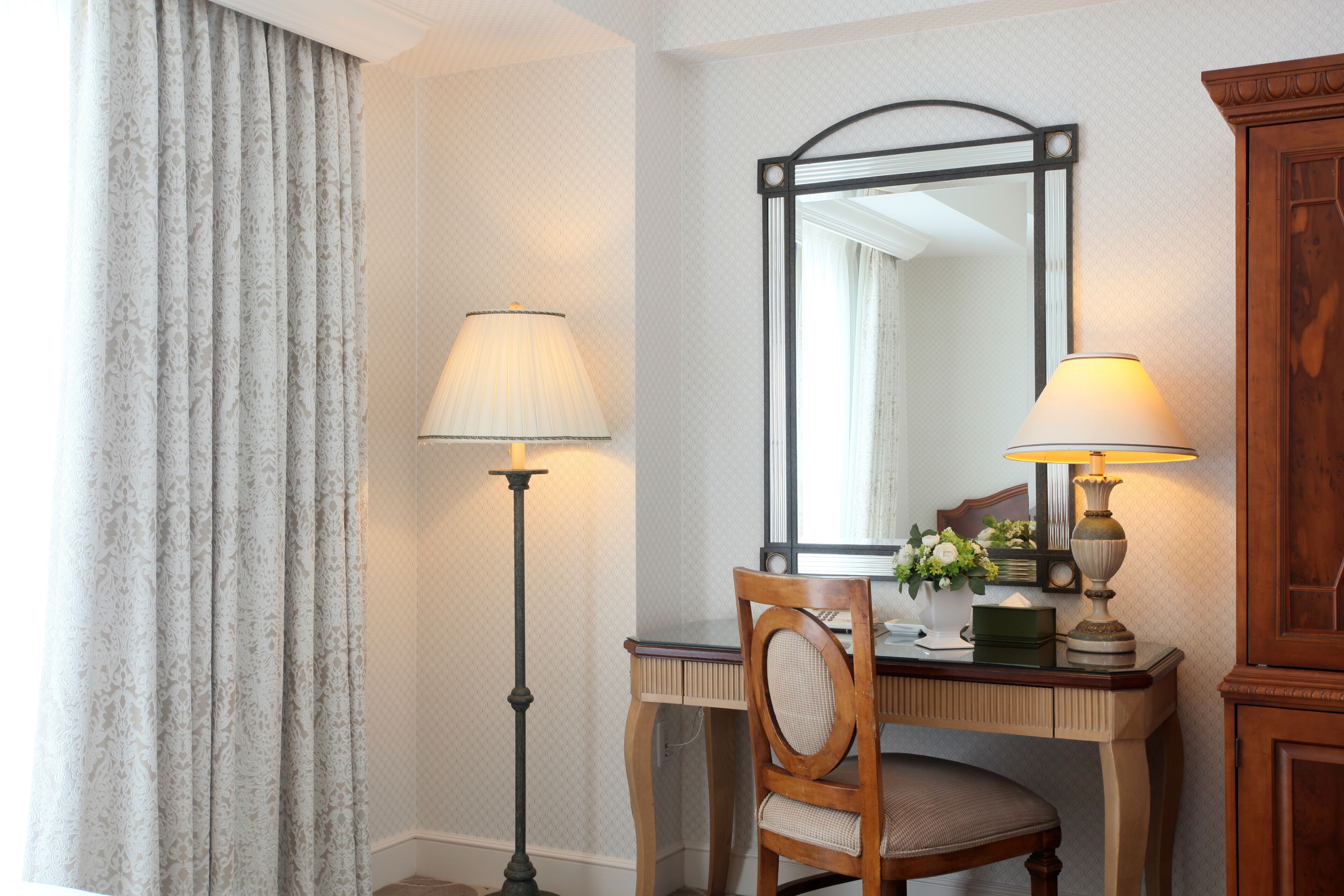 Una habitación de hotel con escritorio, silla, lámpara, espejo y cortinas.