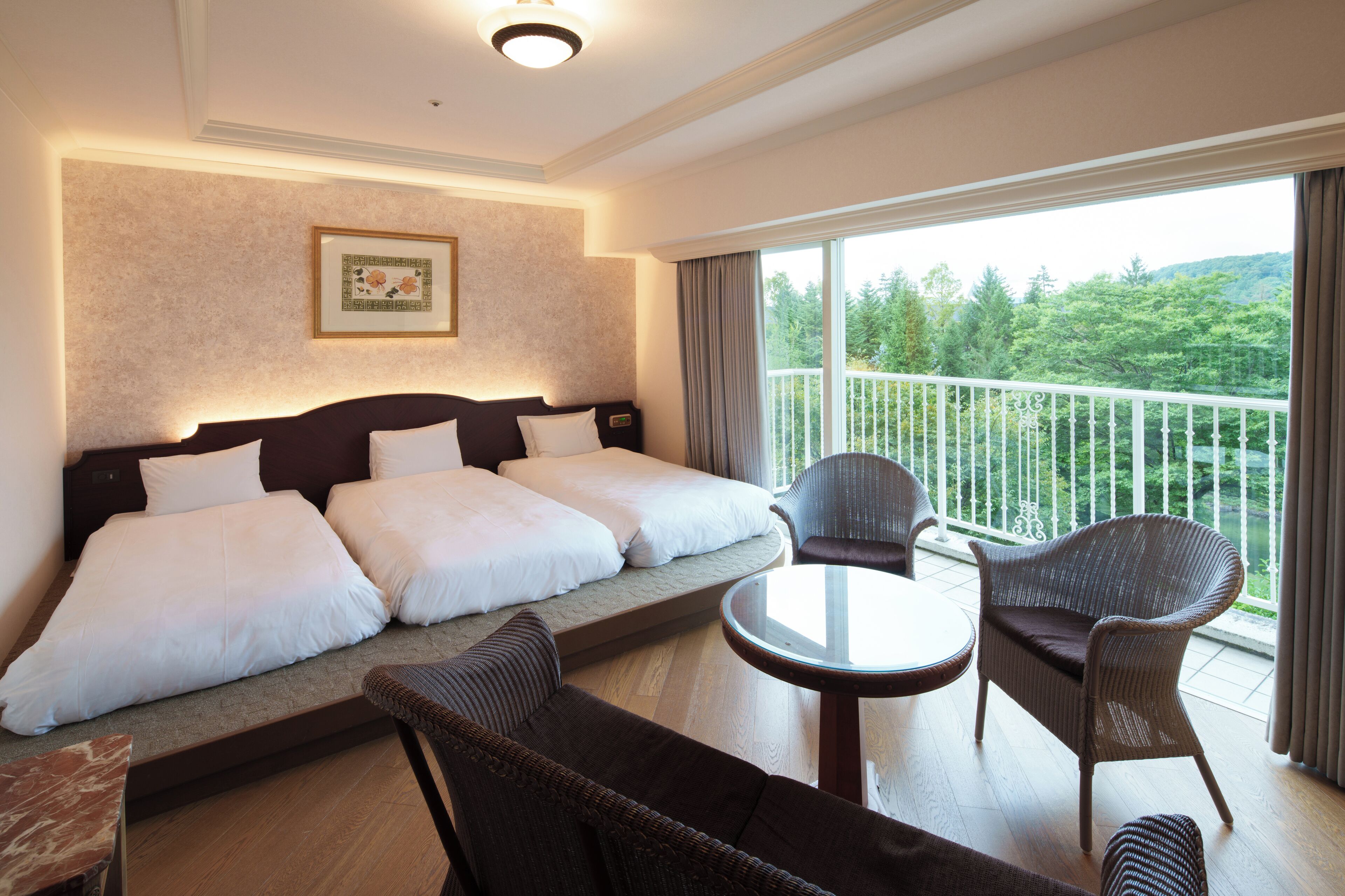 Hotelkamer met een groot bed, een bank, twee stoelen, een kleine tafel en een balkon met uitzicht op groen.