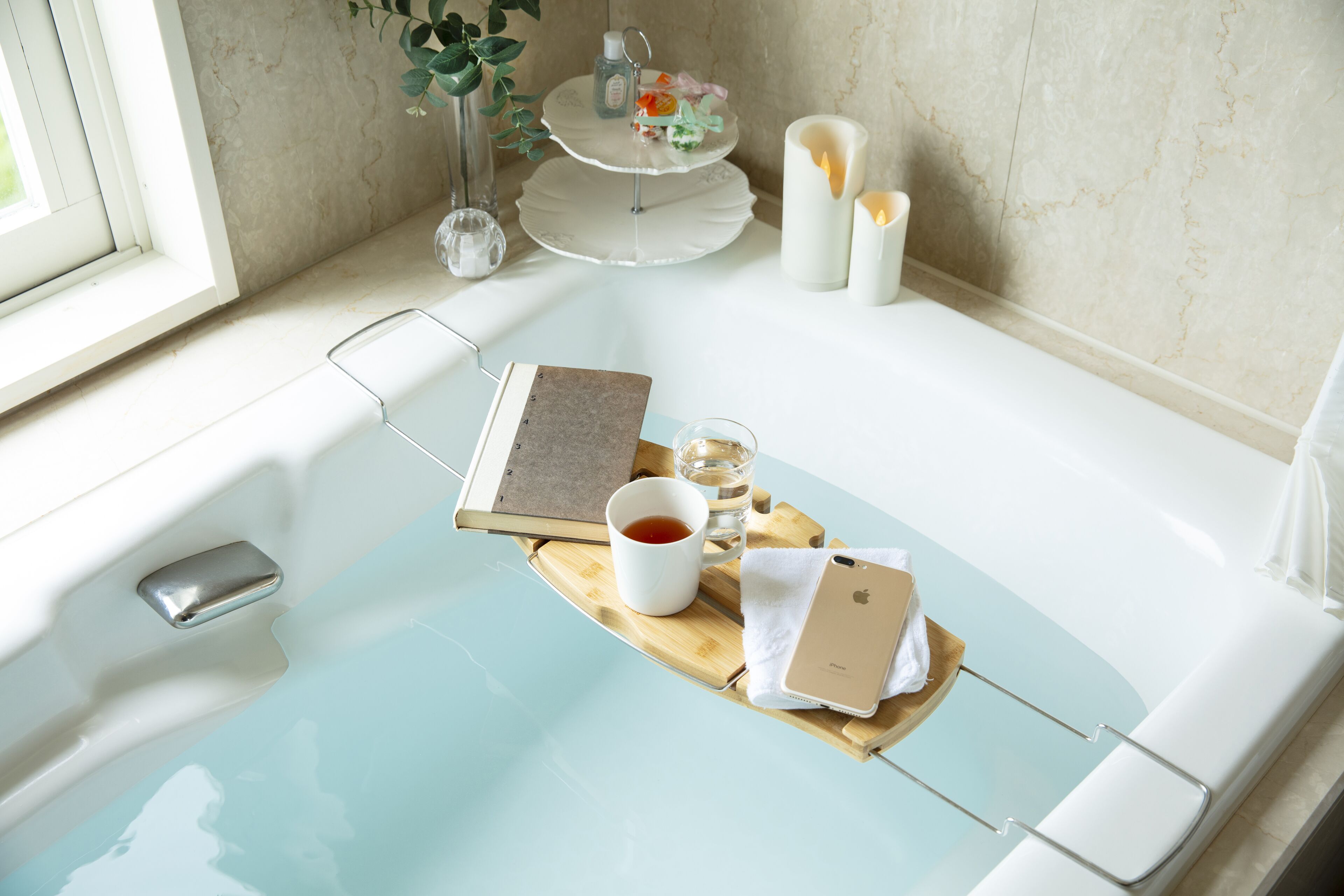 A bathtub with a tray holding a book, a cup, and a tissue.