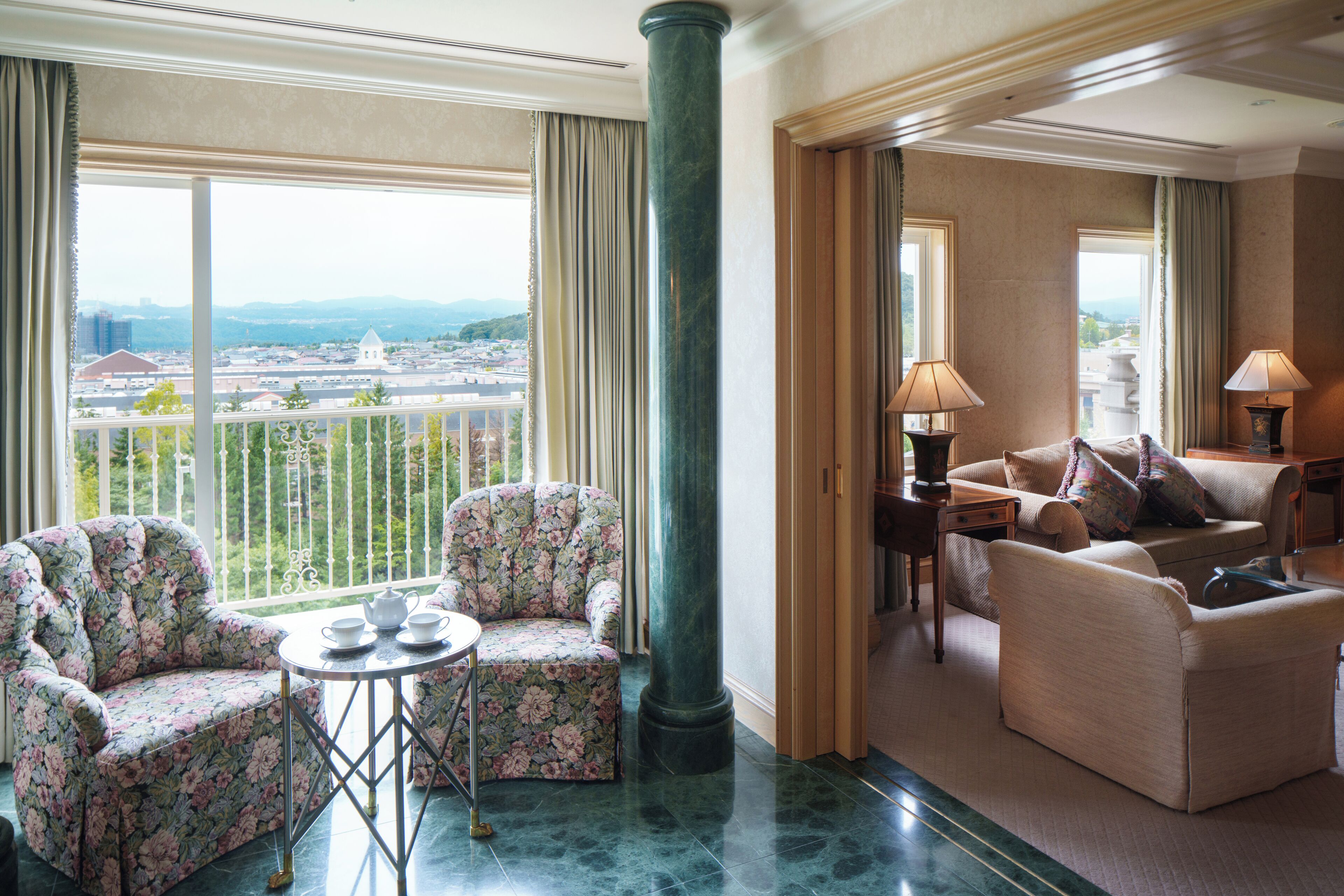A spacious living room with a balcony, a floral armchair, a sofa, and a coffee table.