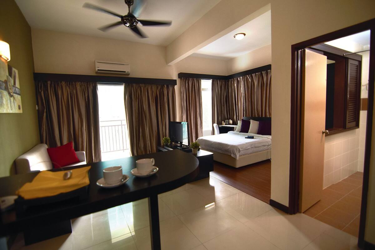 Une chambre d’hôtel avec un lit, un bureau avec une tasse et une soucoupe, un ventilateur de plafond et des rideaux.