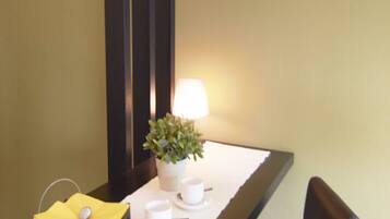 A hotel room with a dining table set for two, a potted plant, and a lamp.