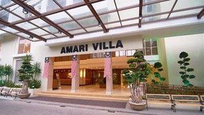 Das Hotel Amari Villa mit Glasfassade, Palmen und einem Schild.