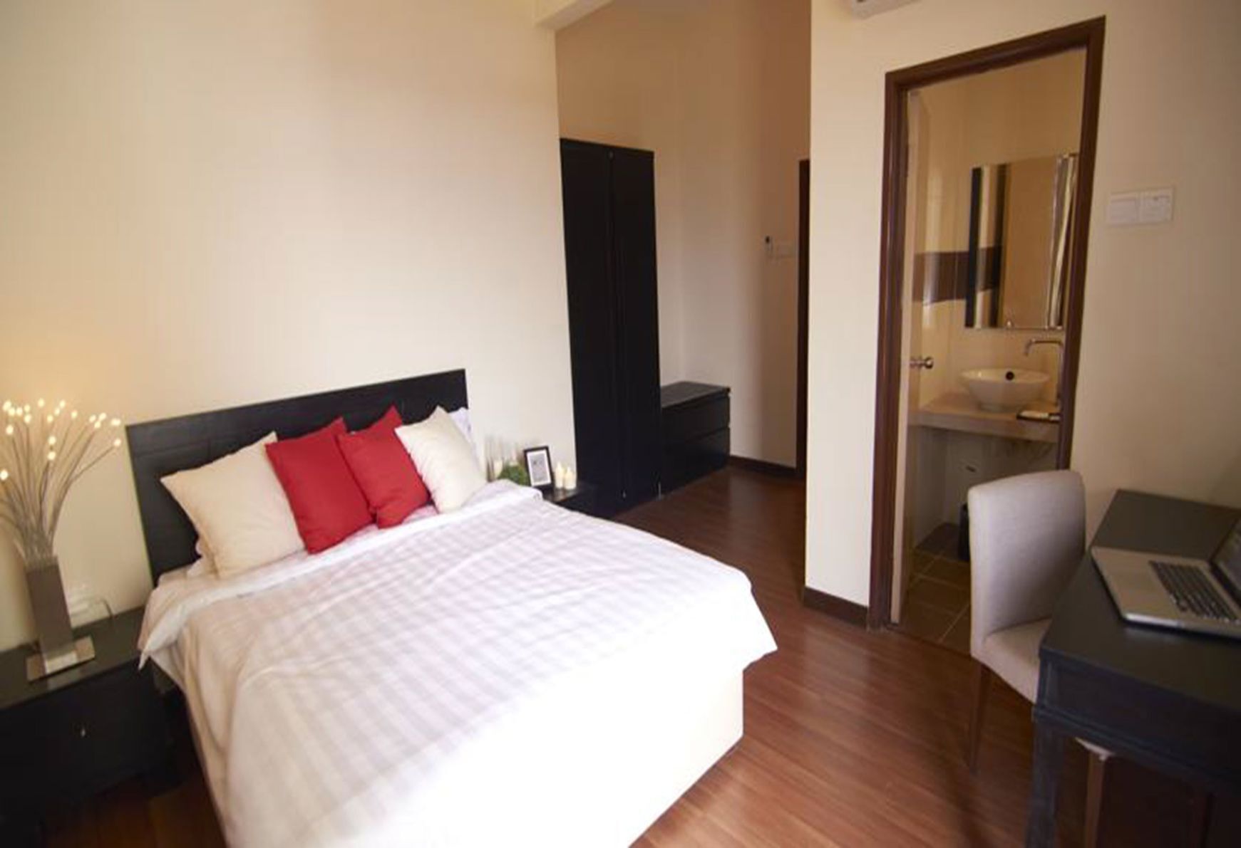 Habitación de hotel con cama, escritorio con una computadora portátil, baño con lavamanos y puerta que da a otra habitación.