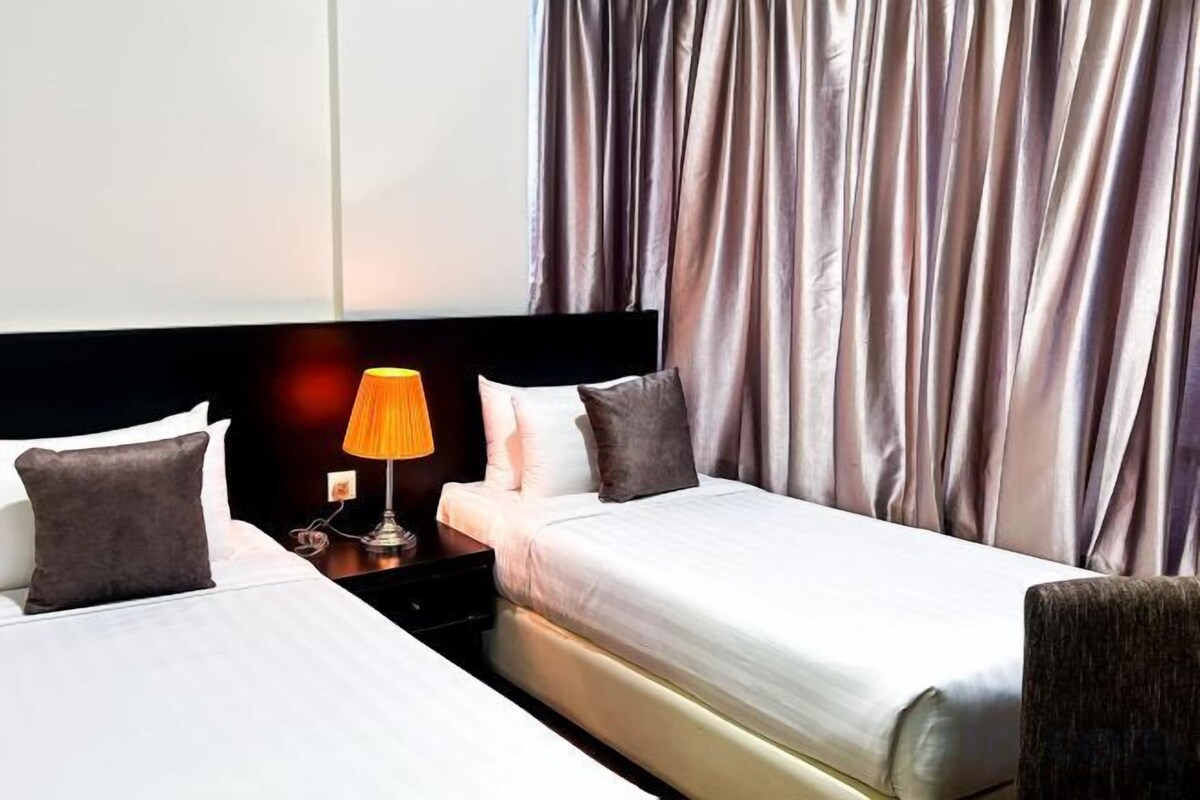 Une chambre d’hôtel avec deux lits, une table de chevet avec une lampe et une vue sur des rideaux.