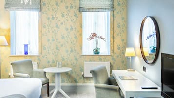 A hotel room with a bed, two armchairs, a small table, a TV, and a window with a plant.