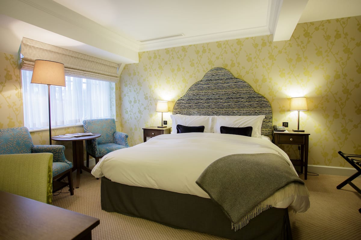 A hotel room with a large bed, two bedside tables with lamps, a chair, and a small table.