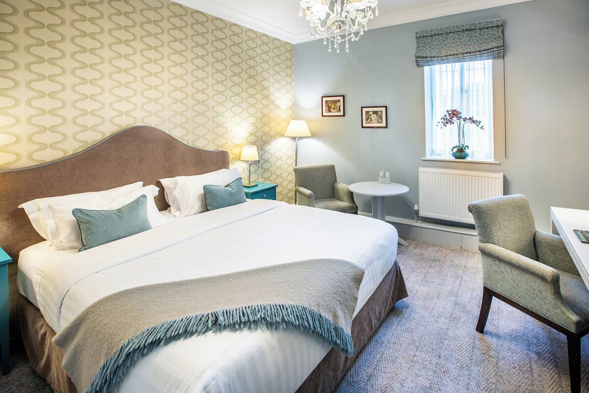 A hotel room with a large bed, a chair, a small table, and a window with a view.