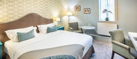 A hotel room with a large bed, a chair, a small table, and a window with a view.