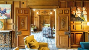 Un vestíbulo amplio con piso estampado, paneles de madera y una variedad de asientos, incluyendo un sillón amarillo y un sofá azul.