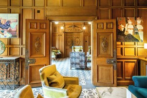 A spacious lobby with a patterned floor, wooden paneling, and a mix of seating including a yellow armchair and a blue sofa.