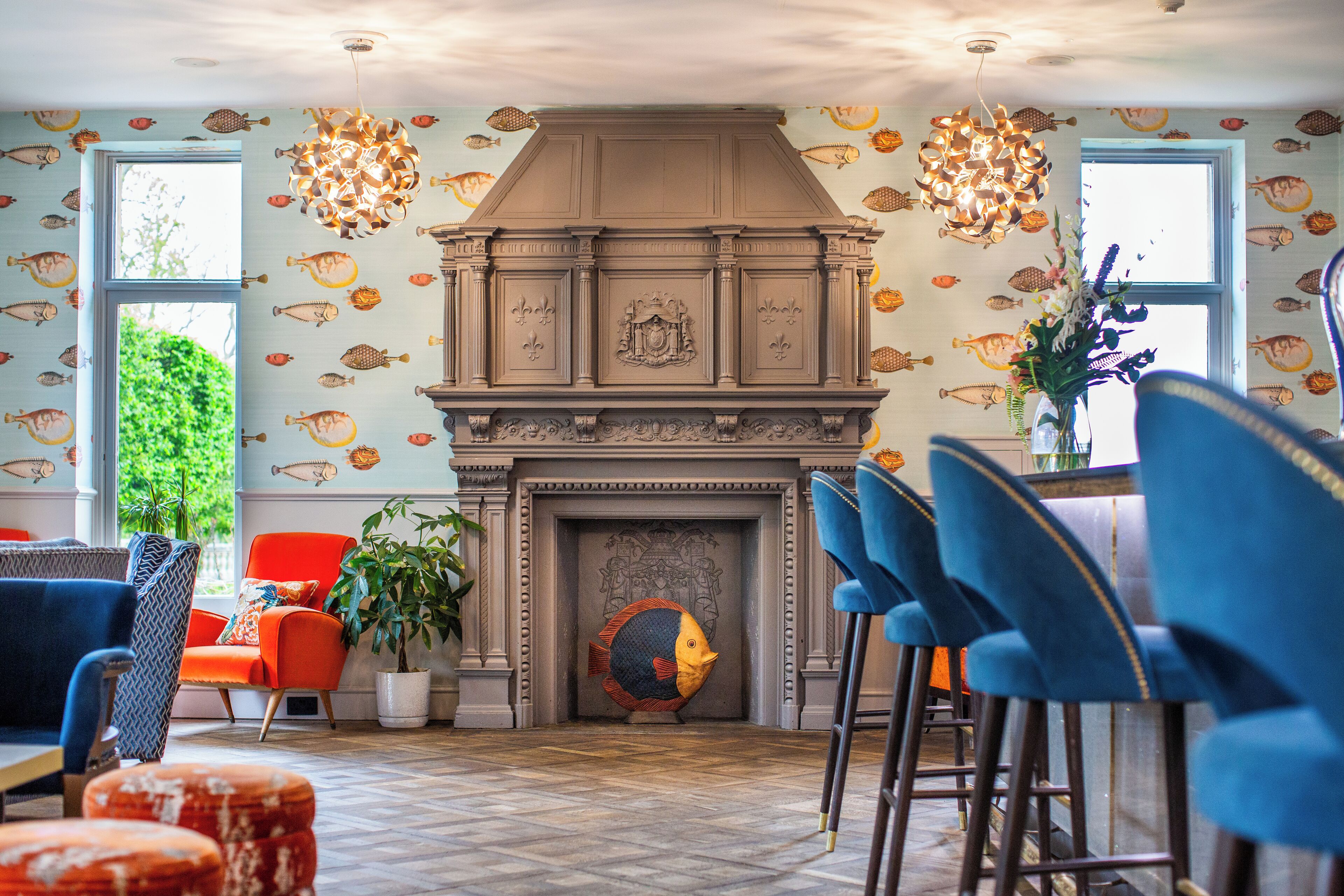 A room with a fireplace, fish-patterned wallpaper, and blue chairs.