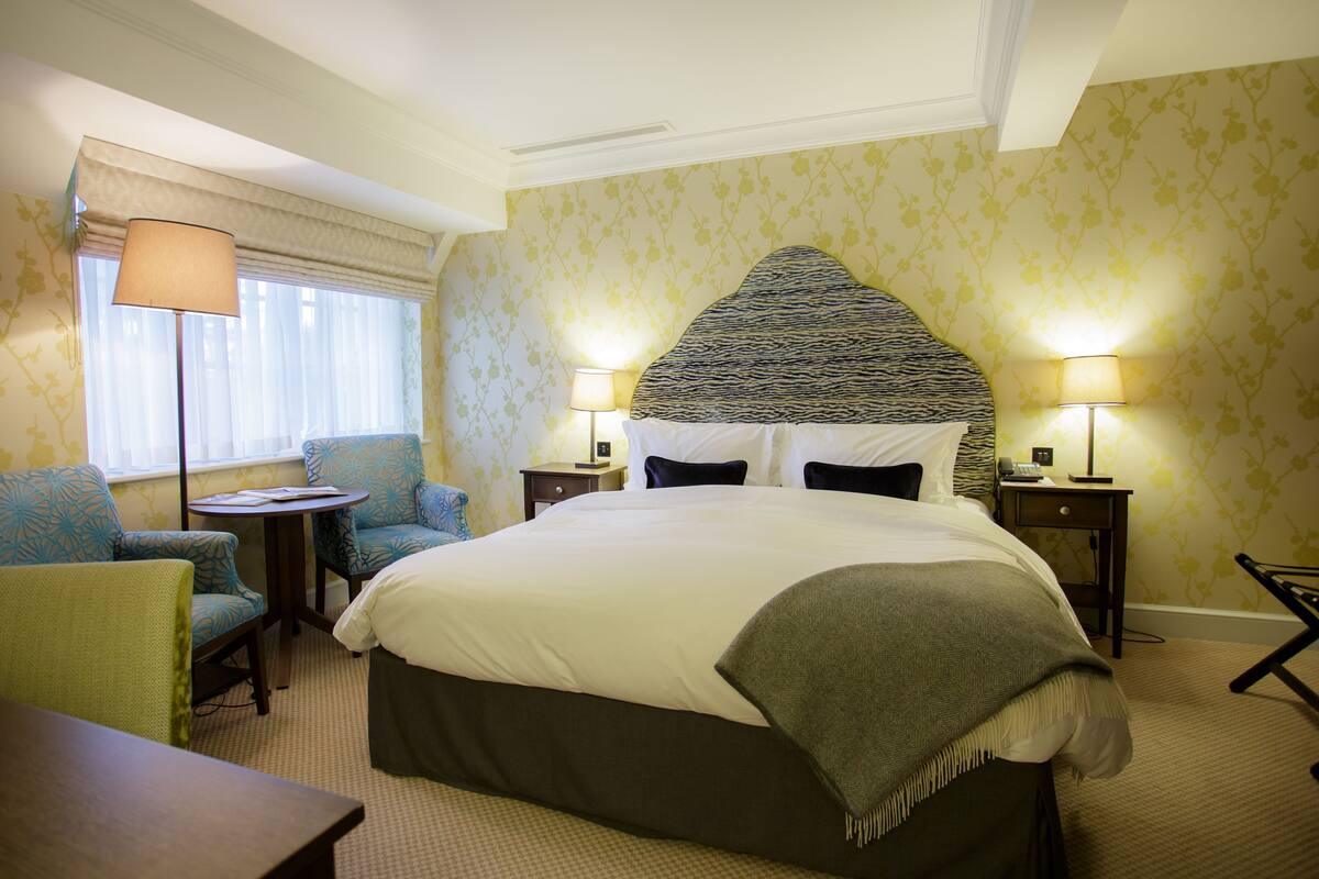 A hotel room with a large bed, two bedside tables with lamps, a chair, and a small table.