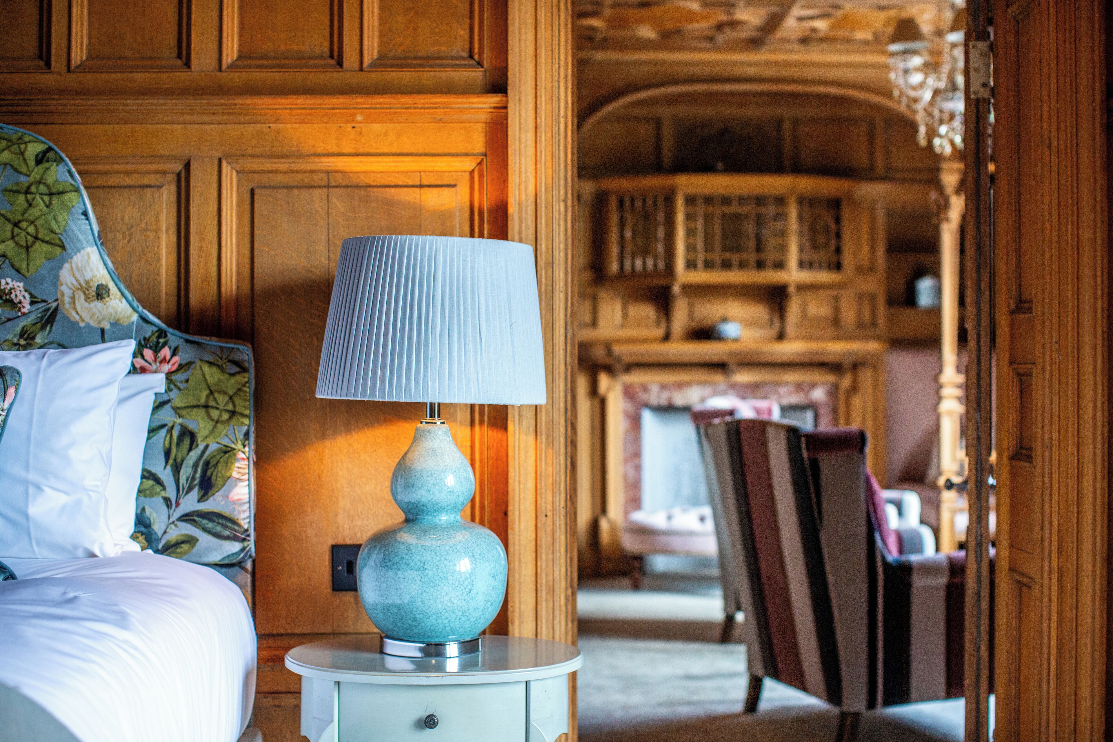 A bedroom with a bed, a nightstand with a lamp, wooden paneling, and a chair.