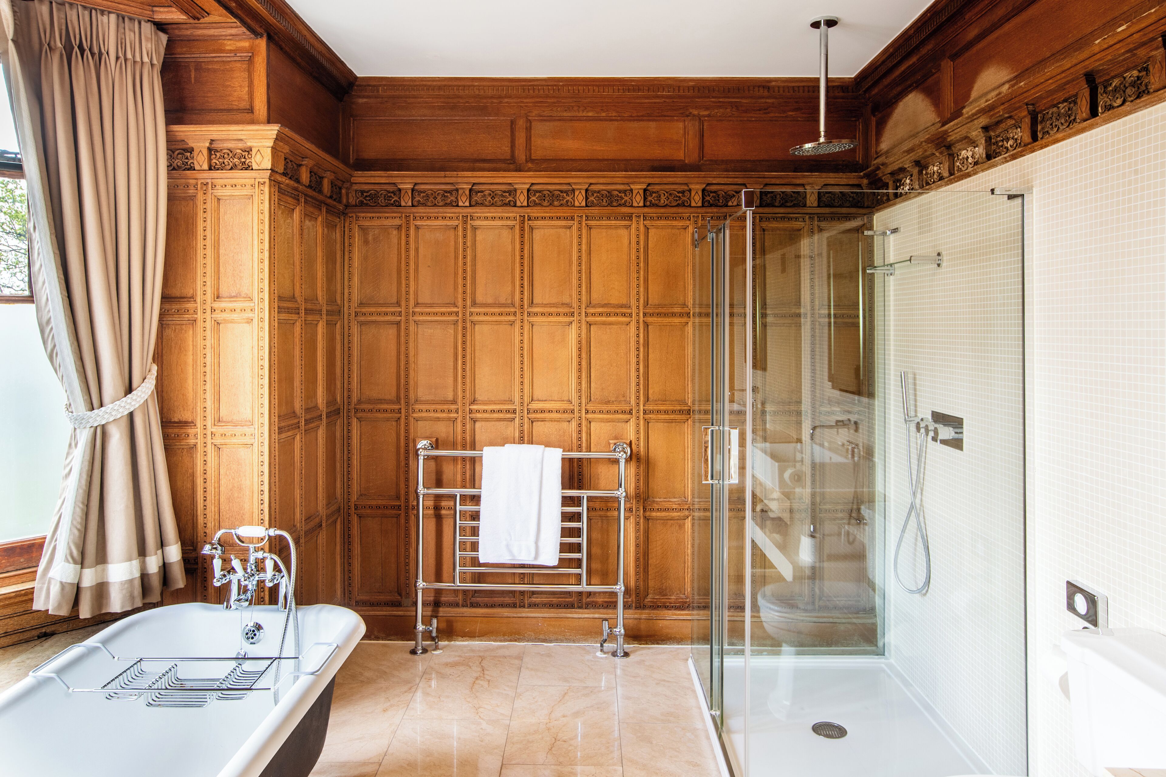 A bathroom with a freestanding bathtub, a glass-enclosed shower, and wooden paneling.
