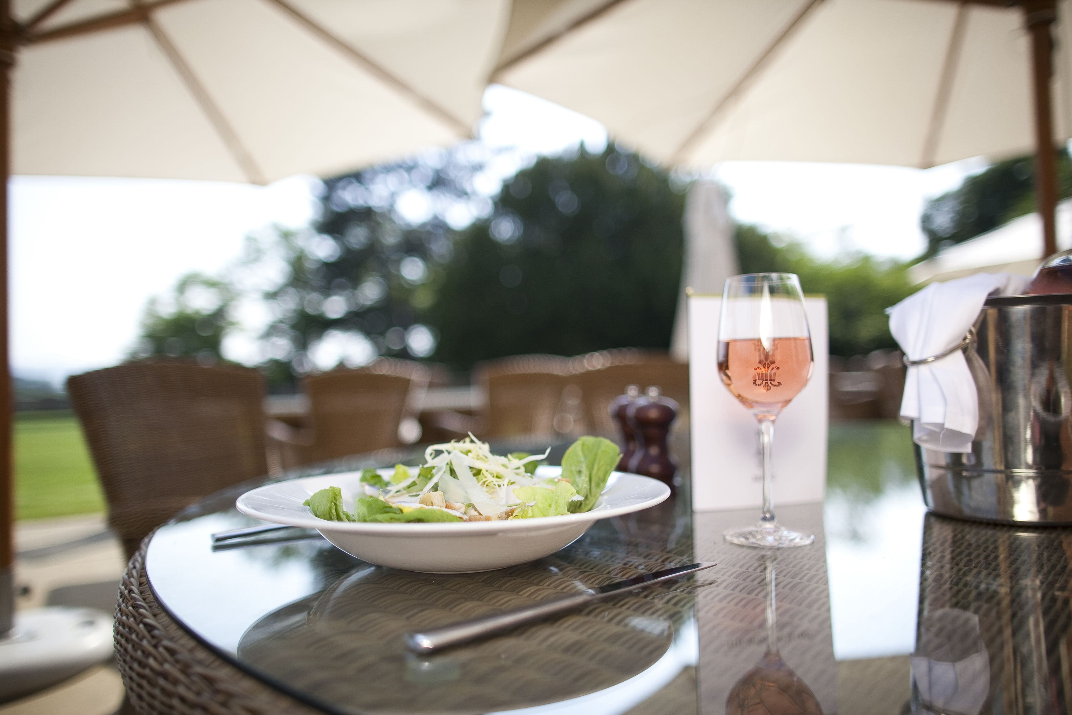 A table with a salad, a wine glass, and a metal pitcher.