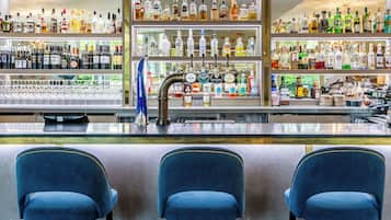 A bar area with multiple shelves of liquor bottles, a tap bar, and three blue chairs.