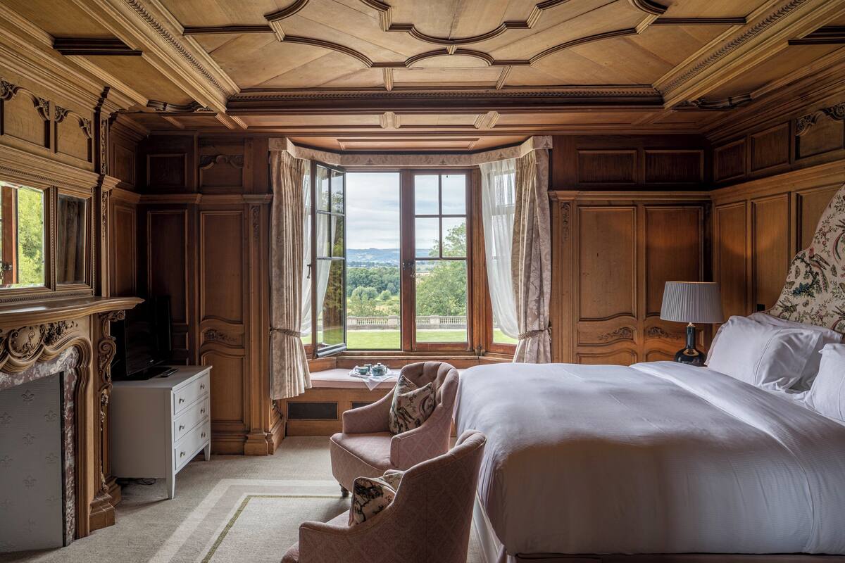 A room with a large bed, a desk, and a window with curtains.