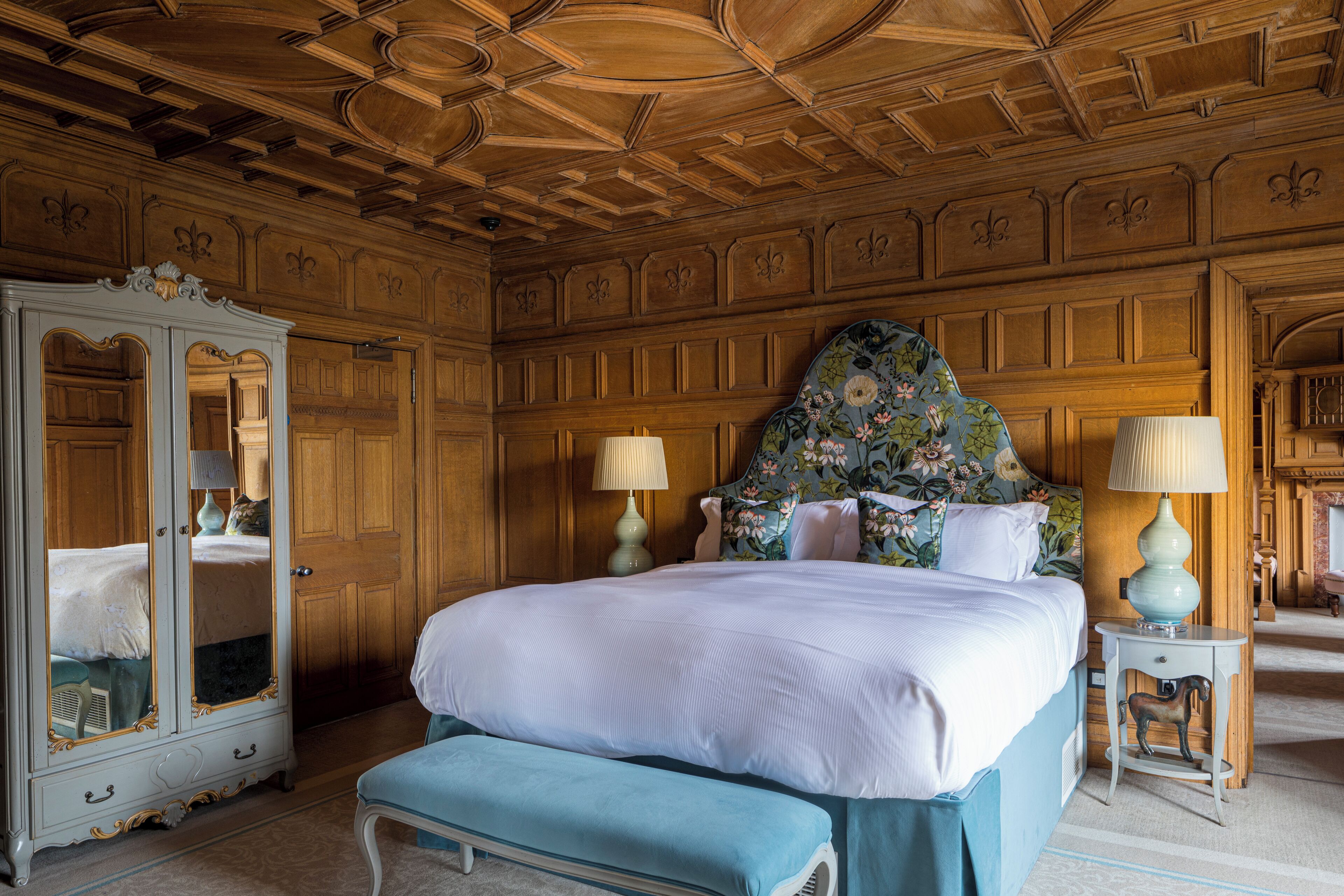 A bedroom with a large bed, a wooden wardrobe, and a floral headboard.