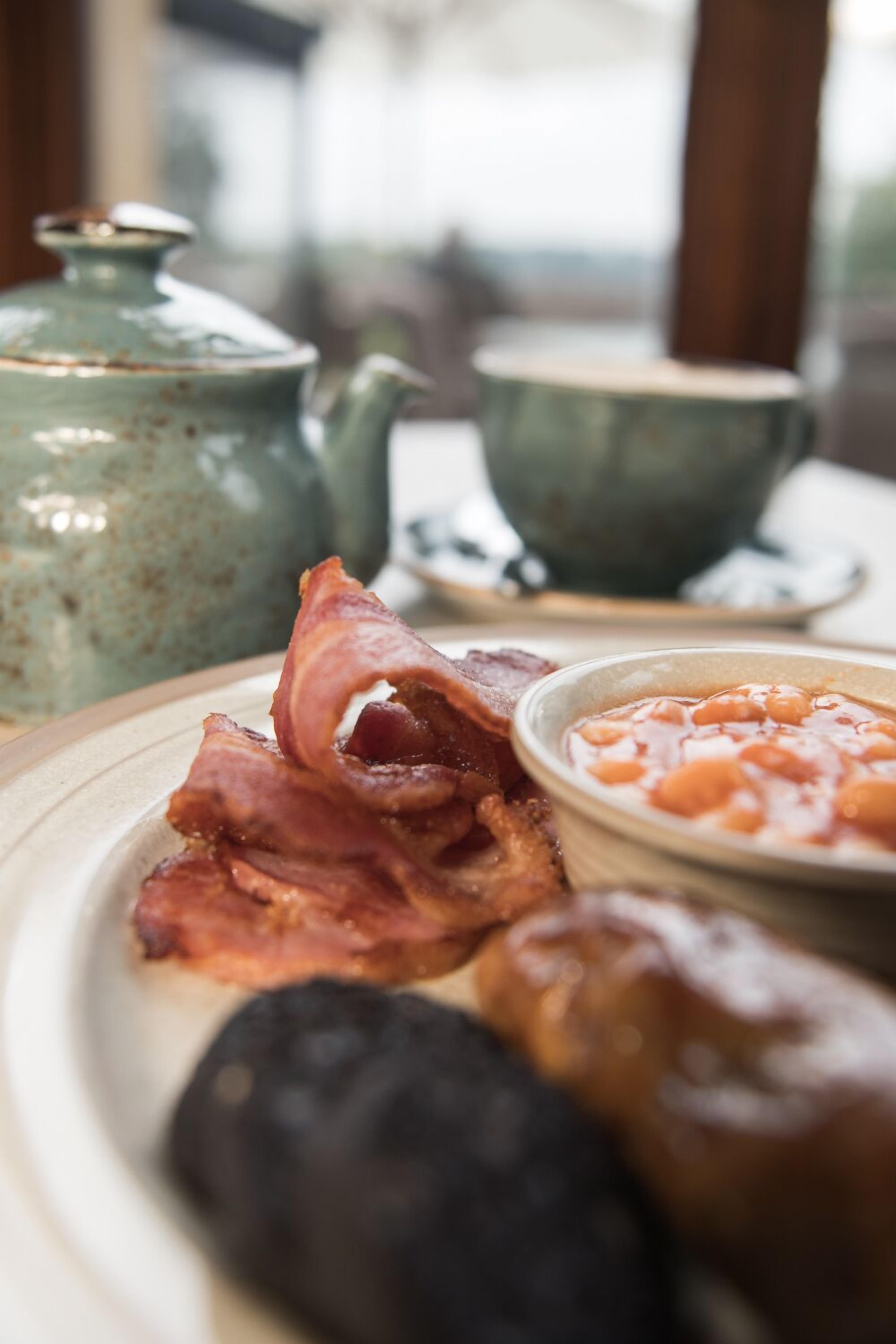 A breakfast tray with bacon, beans, and a teapot.