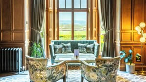 Un rincón acogedor con un sofá y dos sillones, una mesa y vistas a un paisaje verde a través de amplios ventanales.