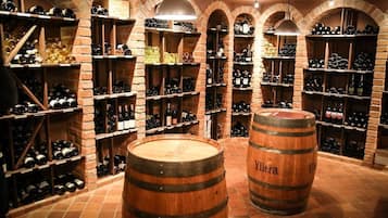 A wine cellar with wooden barrels and shelves of wine bottles.