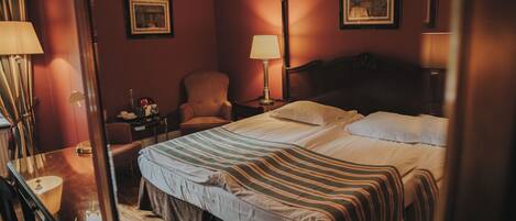 Quarto de hotel com cama, poltrona, escrivaninha e abajur.
