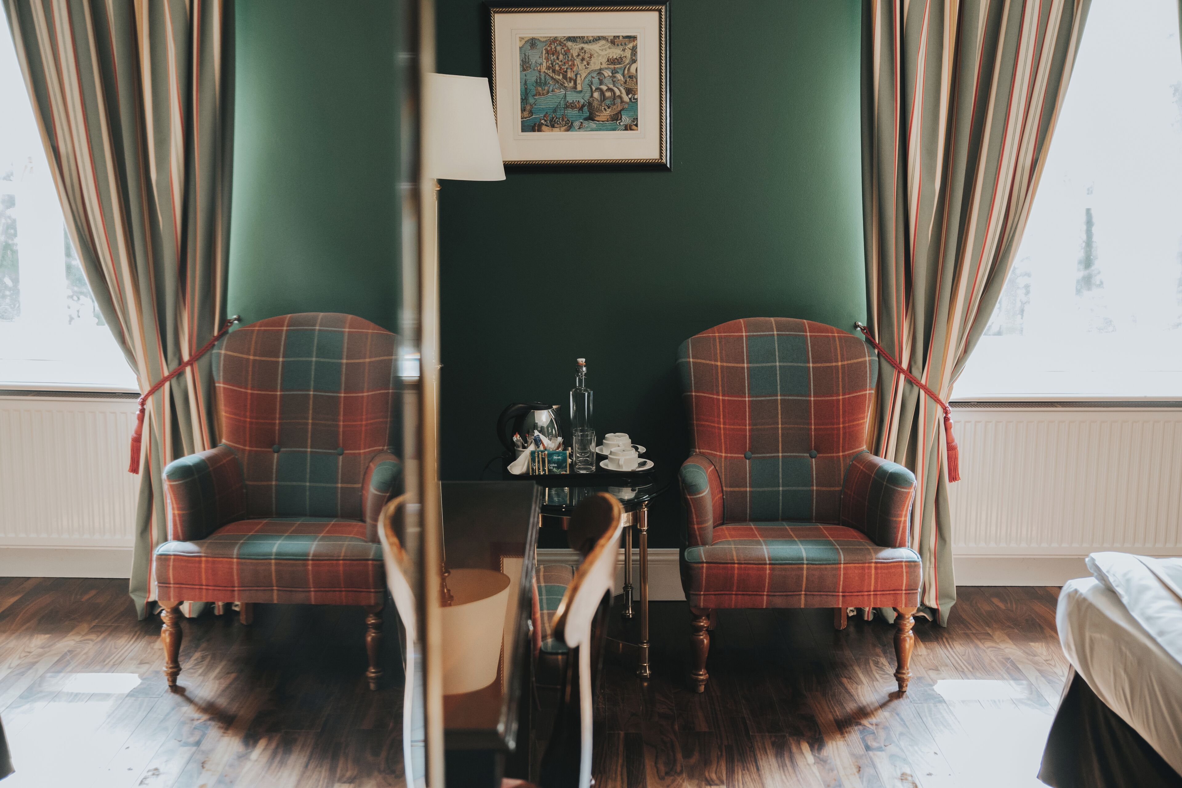 Una habitación con dos sillones a cuadros, una mesita con lámpara y un cuadro enmarcado en la pared.