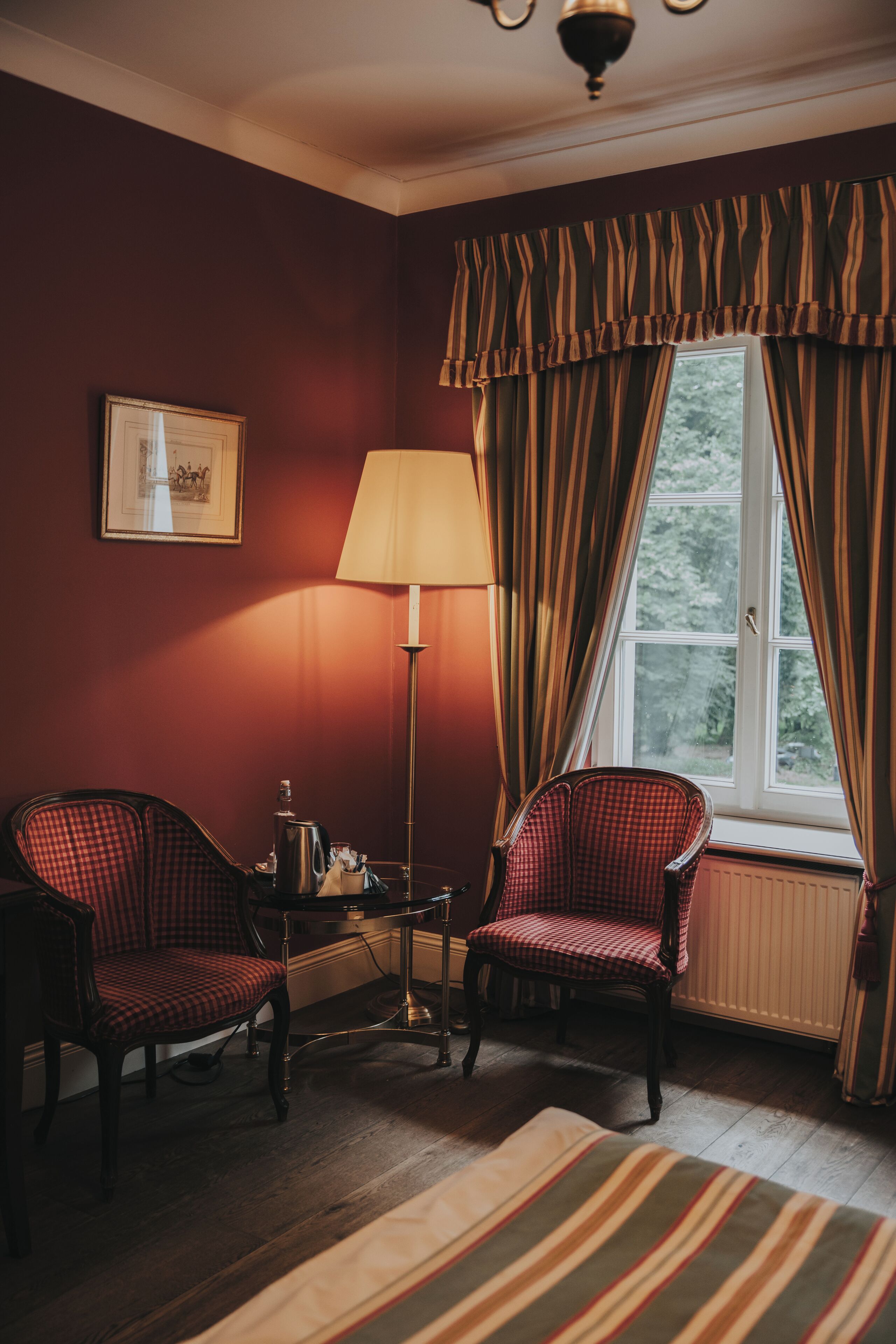 Una habitación con dos sillones, una lámpara de pie y un ventanal con cortinas.