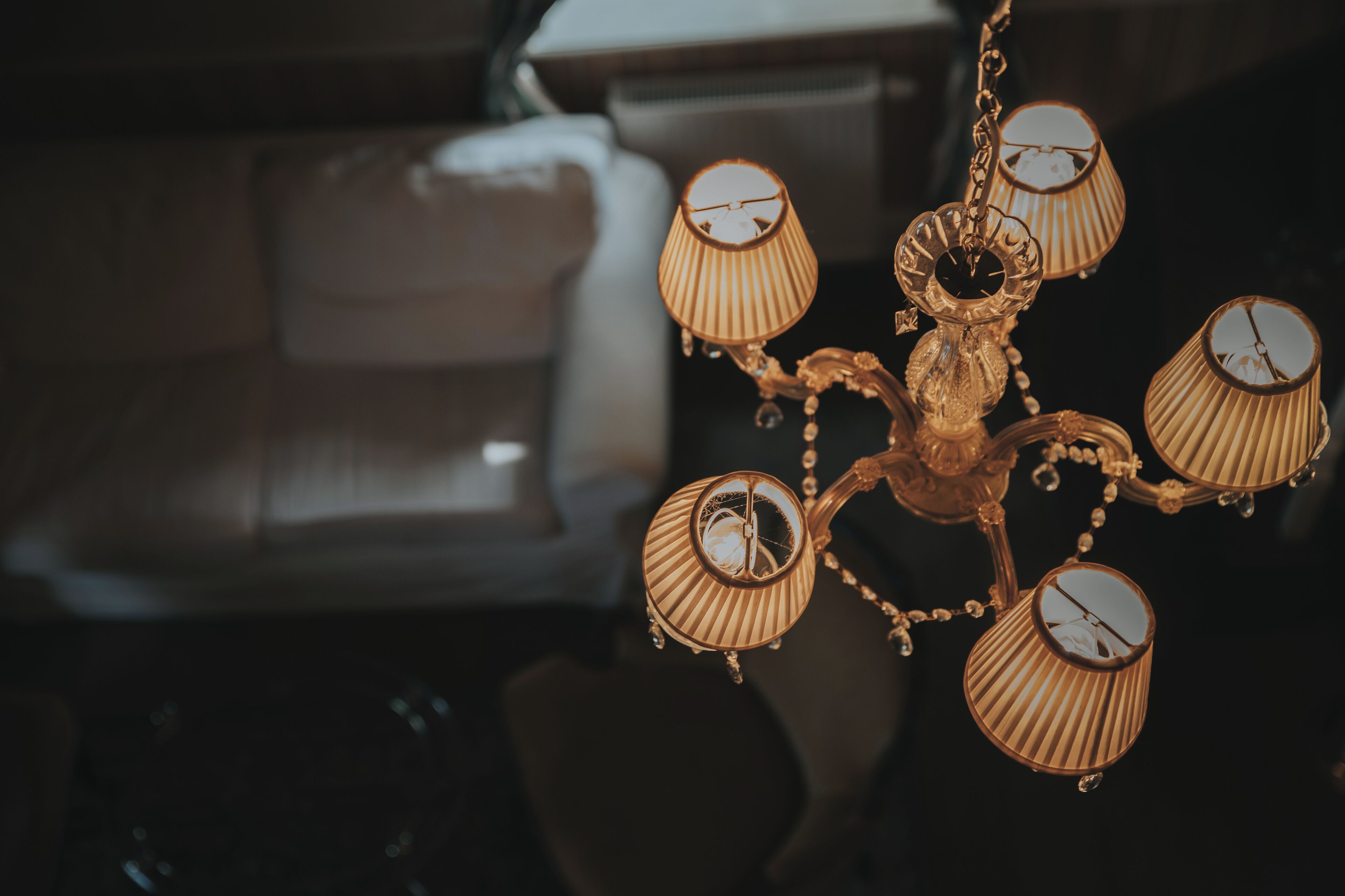 A chandelier with multiple lampshades in a dimly lit room with a sofa in the background.